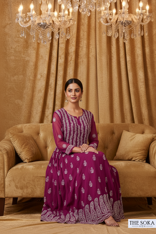 Woman in a purple dress sitting on a beige sofa with chandeliers and curtains in the background.