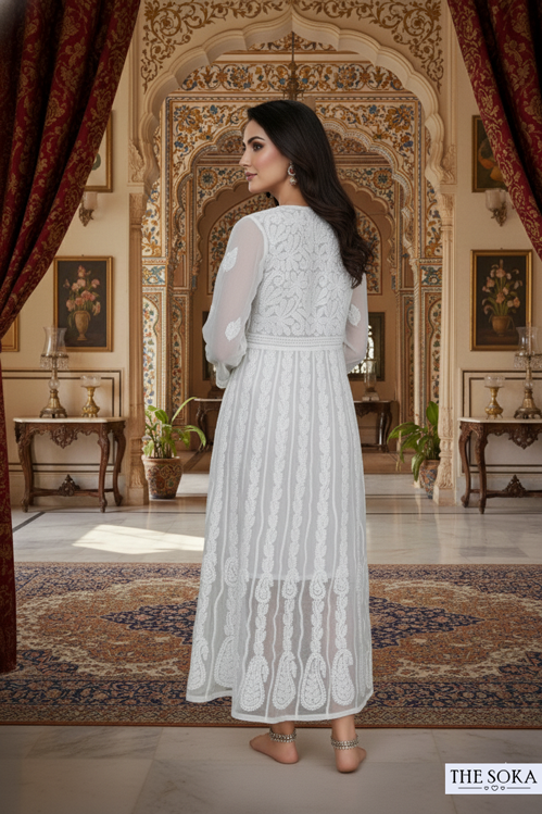 Woman in a white lace dress standing in an ornate room with intricate wall designs and furniture.