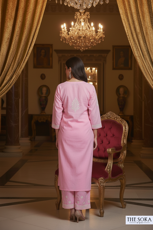 Woman in a pink traditional outfit standing in an opulent room with gold curtains and a chandelier.