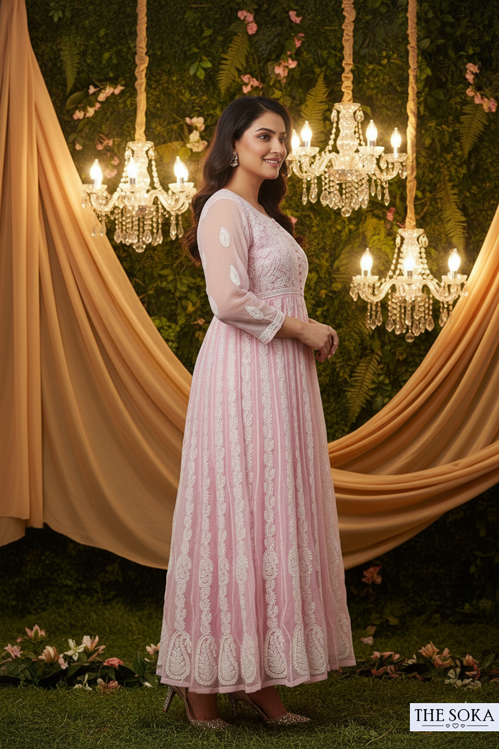 Woman in a pink dress standing in front of decorative chandeliers and draped fabric.