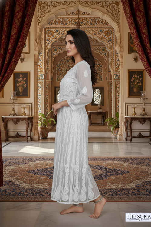 Woman in a white lace dress standing in an ornate room with intricate decor.
