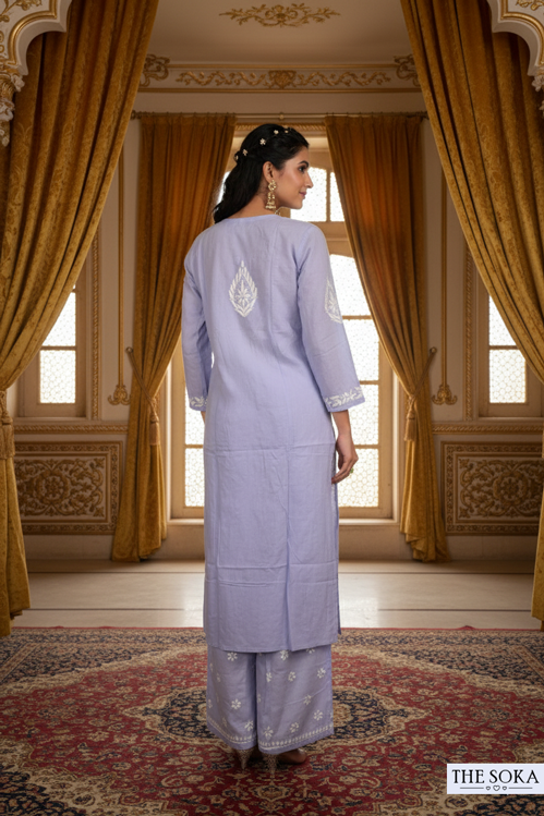 Woman in a lavender traditional outfit standing in an ornate room with gold curtains.