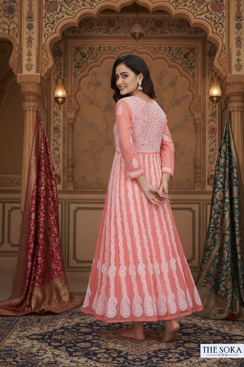 Woman in a pink and white traditional outfit standing in an ornate room with decorative walls.