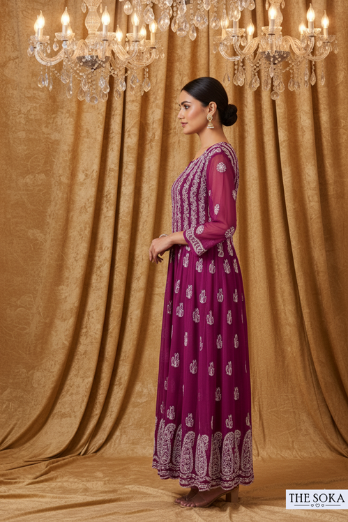 Woman in a purple dress with white patterns standing in front of a chandelier and gold curtains.