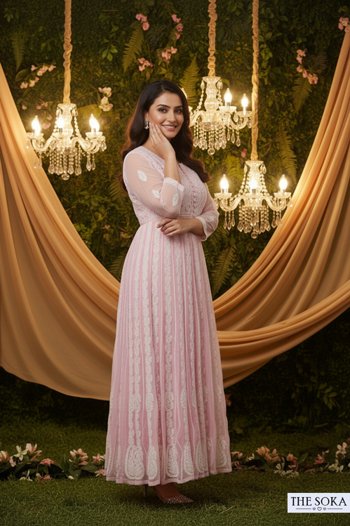 Woman in a pink dress standing in front of decorative chandeliers and draped fabric.