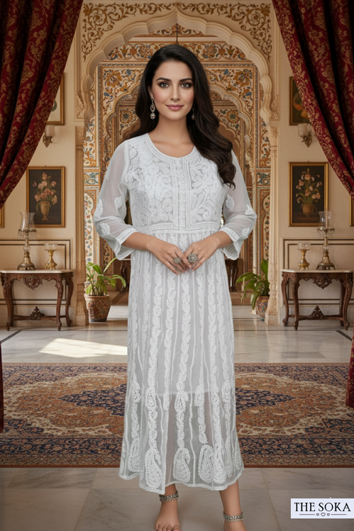 Woman in a white lace dress standing in an ornate room with intricate decor.