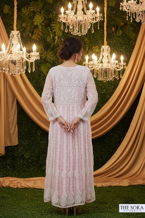 Woman in a pink and white traditional outfit standing in front of chandeliers and draped fabric.