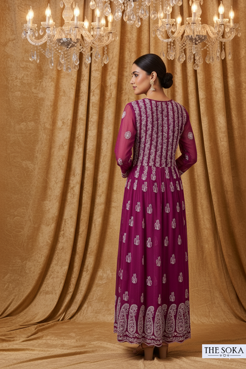 Woman in a purple dress with white patterns standing in front of a chandelier and draped fabric.