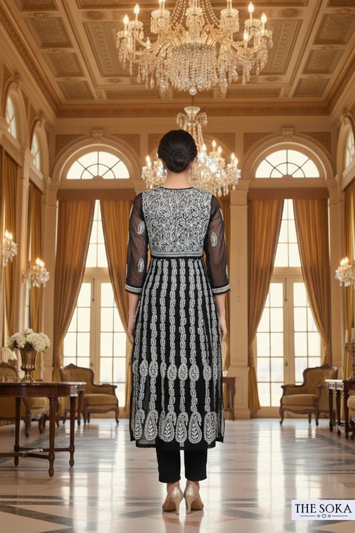 Woman in a black and white patterned outfit standing in an elegant room with chandeliers and large windows.