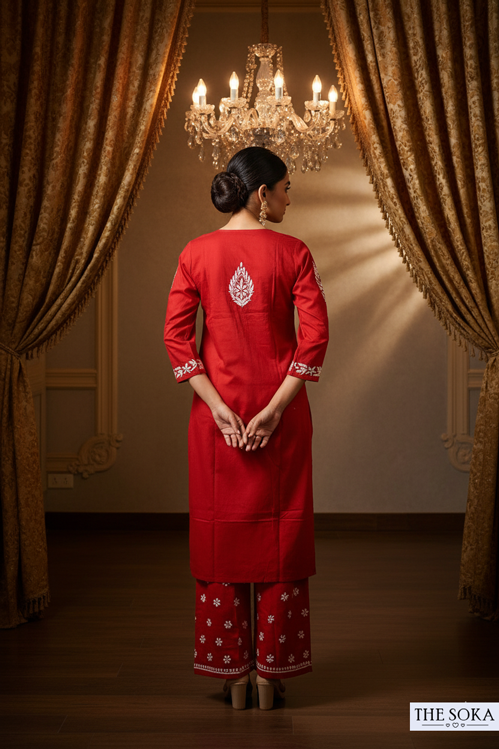 Woman in a red traditional outfit standing in a room with gold curtains and a chandelier.