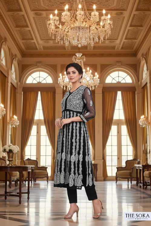 Woman in a black and white patterned dress standing in an elegant room with chandeliers.