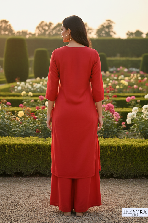 Woman in a red outfit standing in a garden with flowers and greenery.