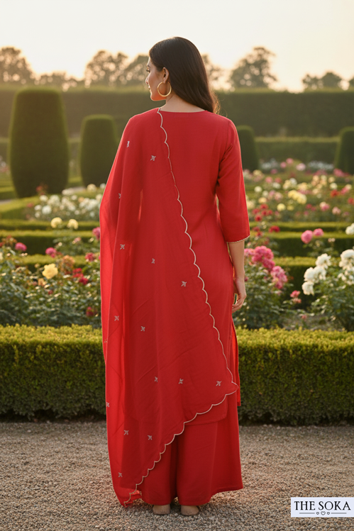 Woman in a red outfit standing in a garden with flowers and trees.