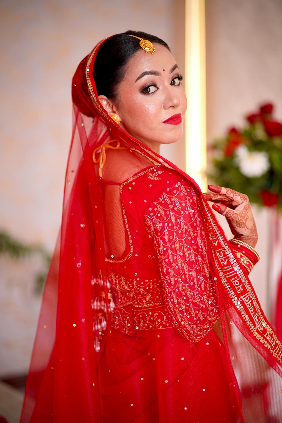 Woman in a red traditional outfit with a veil, posing indoors.